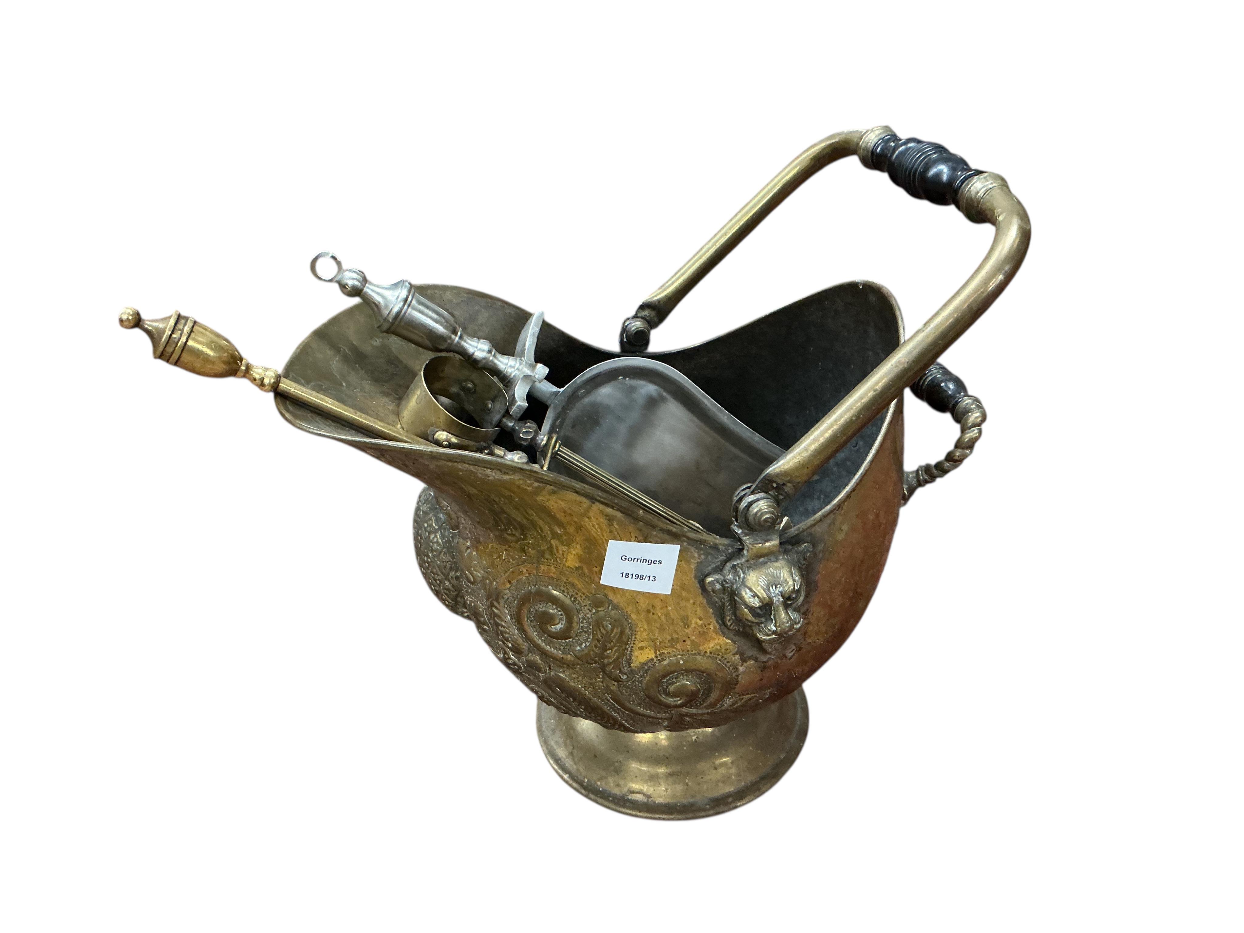 An embossed brass helmet shaped coal scuttle and assorted fire implements